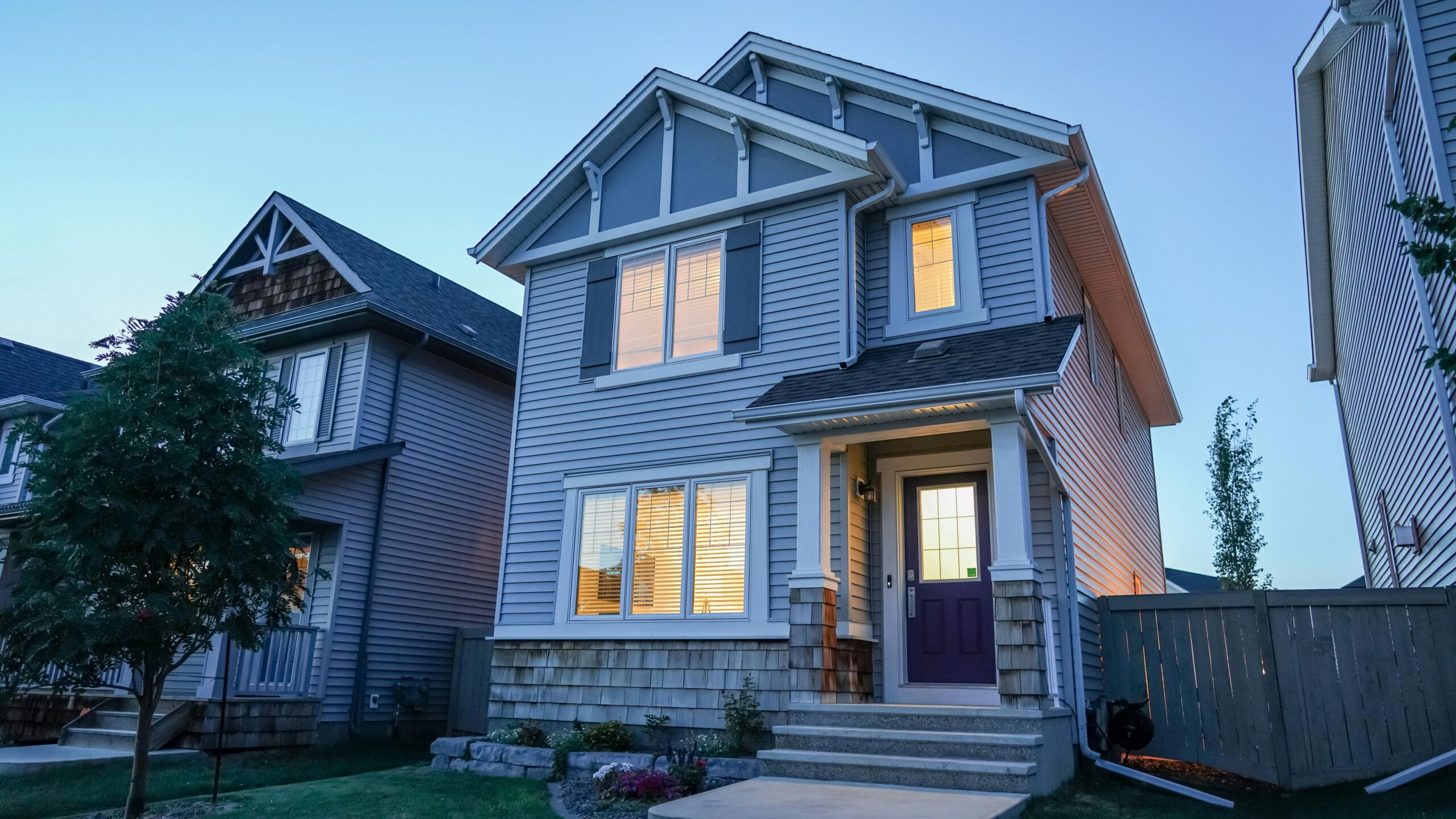 Charming modern suburban house with illuminated windows at dusk, featuring sleek architecture and wooden accents.